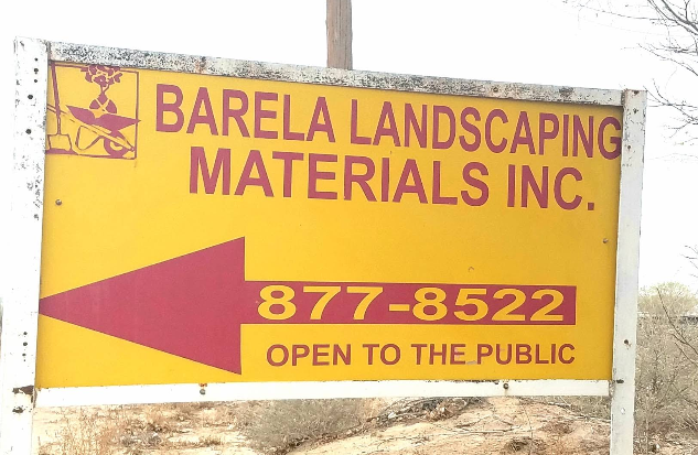 Yellow and maroon Barela Landscaping Materials Inc. roadside sign with shovel, pick, and wheelbarrow logo